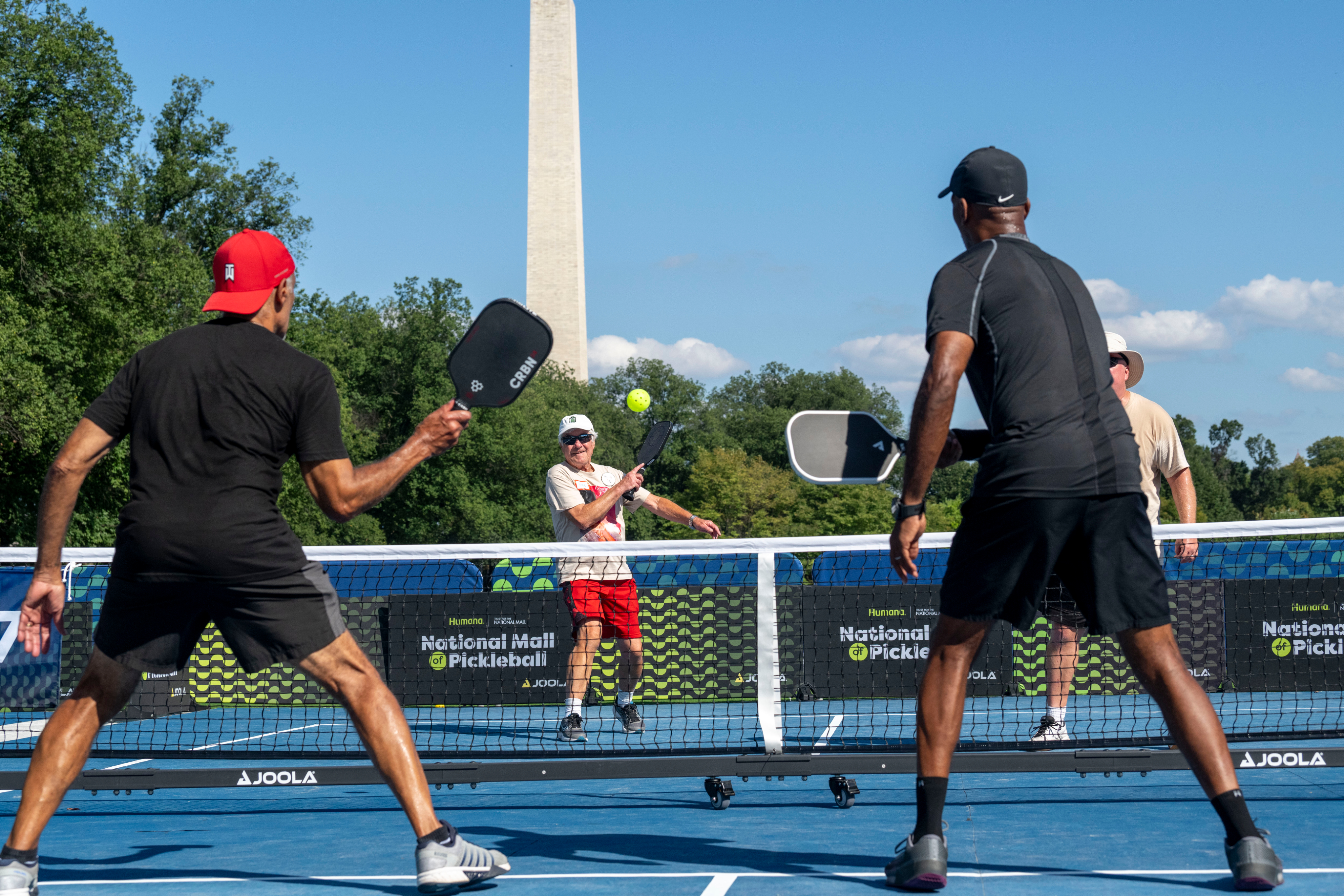 Ongoing pickleball game from behind as a strike is returned.